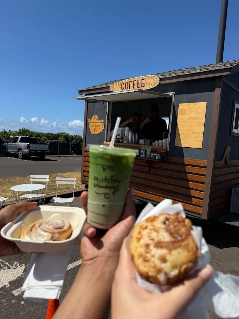 The First Wave Coffee trailer in Kahului on a sunny morning, with an iced matcha and a cinnamon roll held up in front.