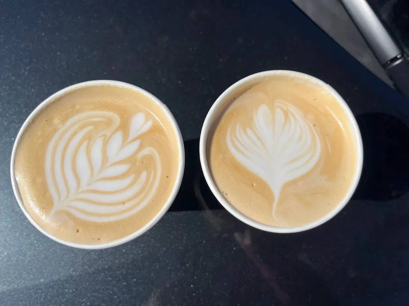 Two lattes with rosetta latte art on a dark counter, seen from above.