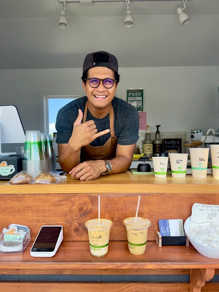 One of the brothers leaning on the trailer counter, throwing a shaka beside fresh espresso drinks.